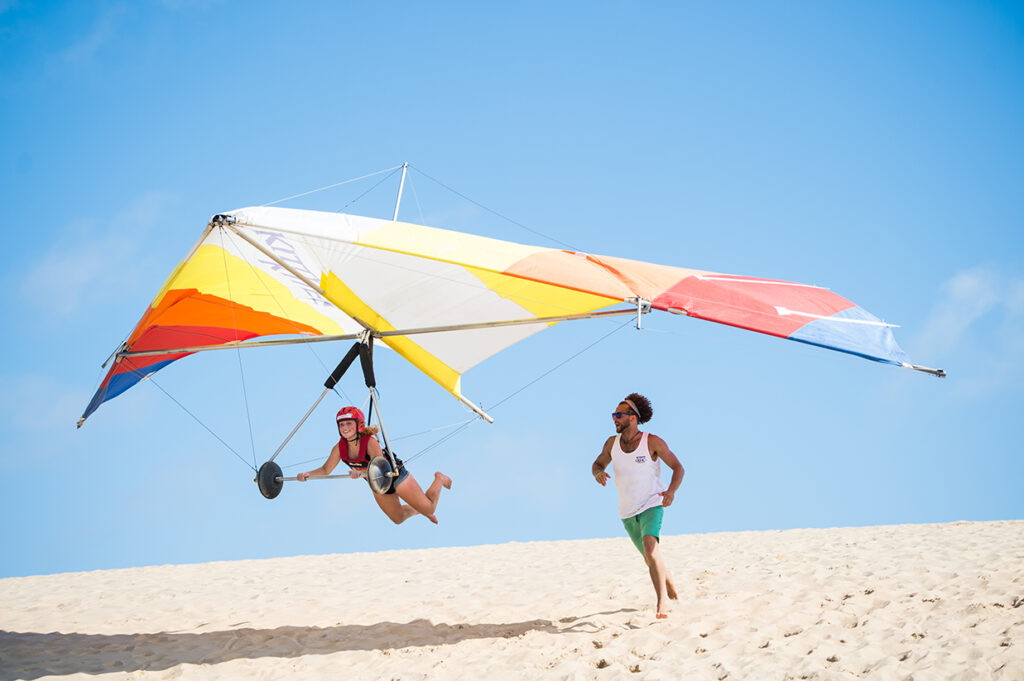 A girl flying a hang glider, a man running beside her