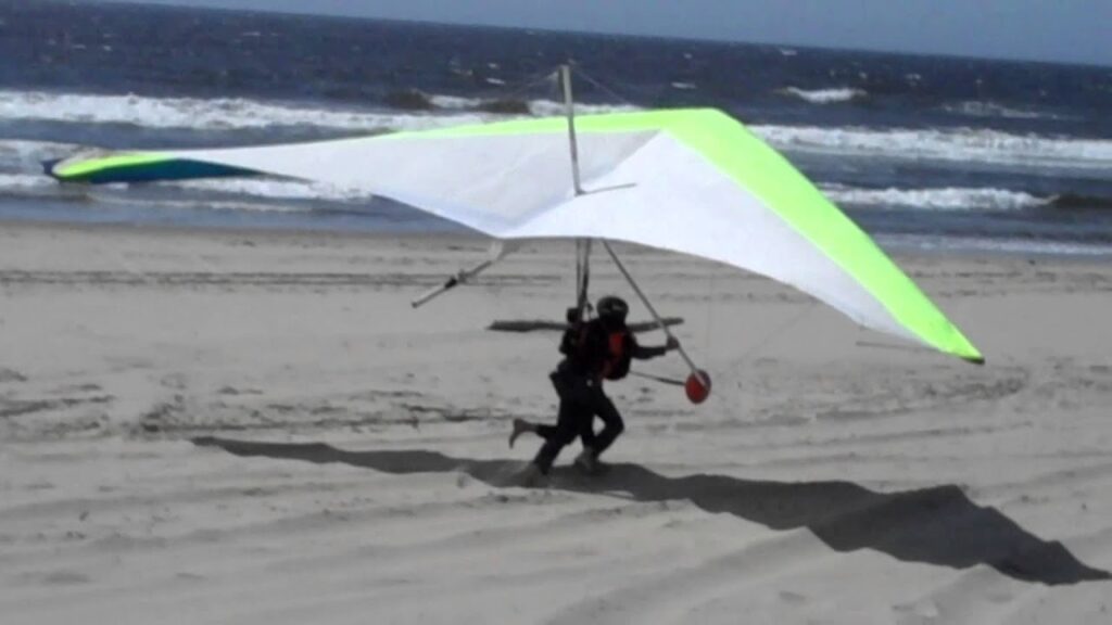 A man walks with a hang glider along the seashore