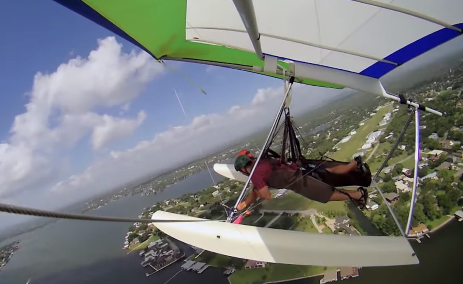 A hang glider pilot maneuvering the glider high above an urban lakeside area with clear skies