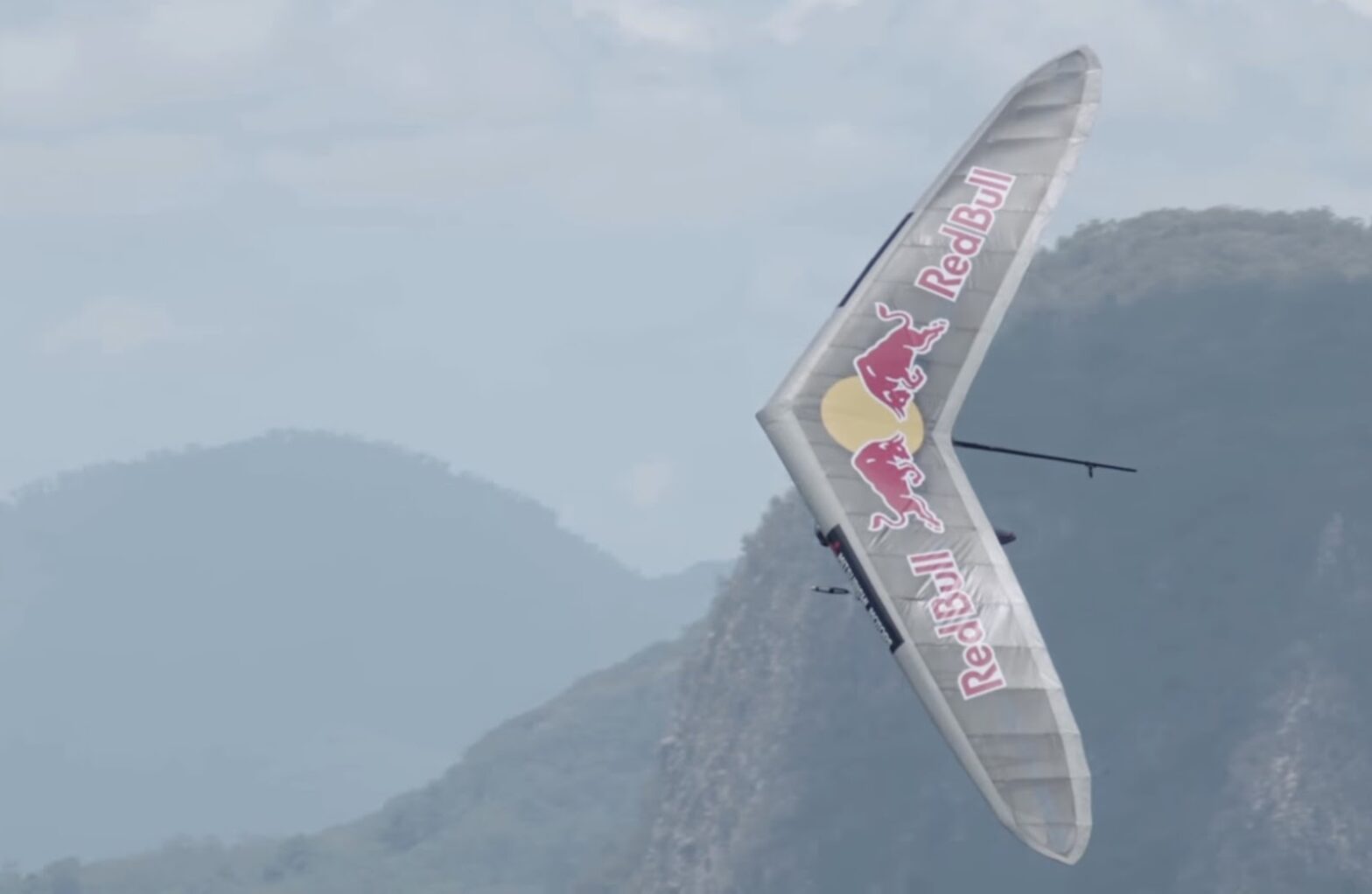 A hang glider adorned with Red Bull logos flying high above hazy mountain ridges