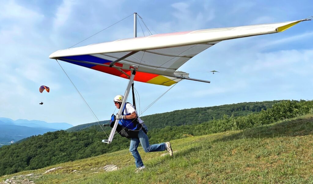 A man runs along the mountain with a hang glider