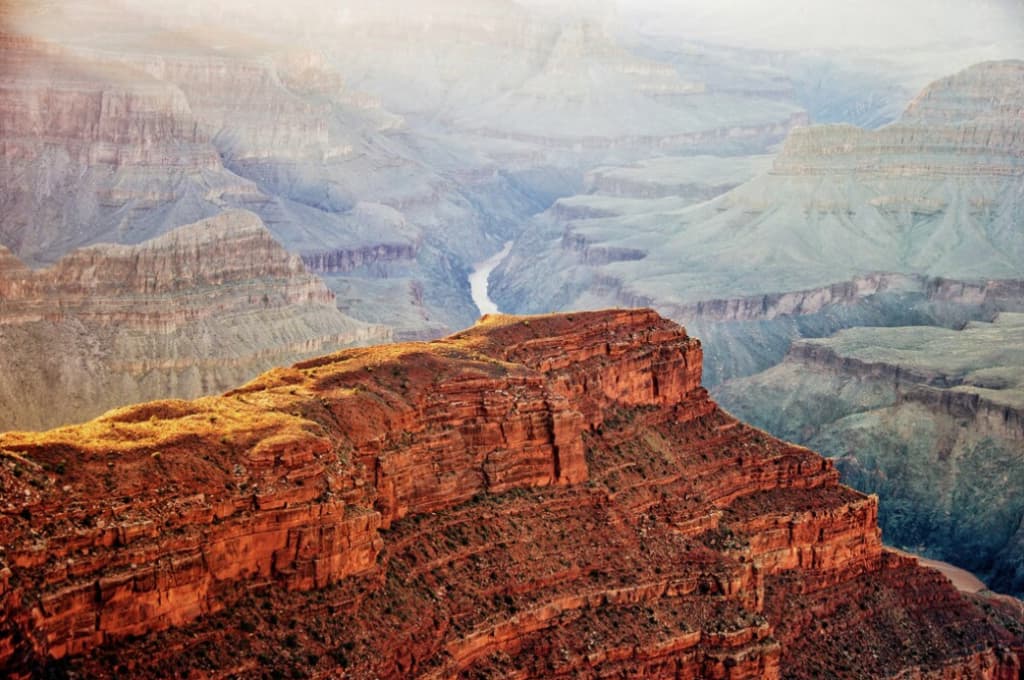 A view of the Grand Canyon with layered rock formations and a river carving through the valley