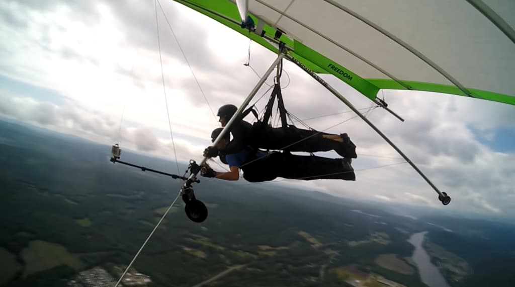 Hang glider in flight with a camera attached, overlooking a vast landscape with a river