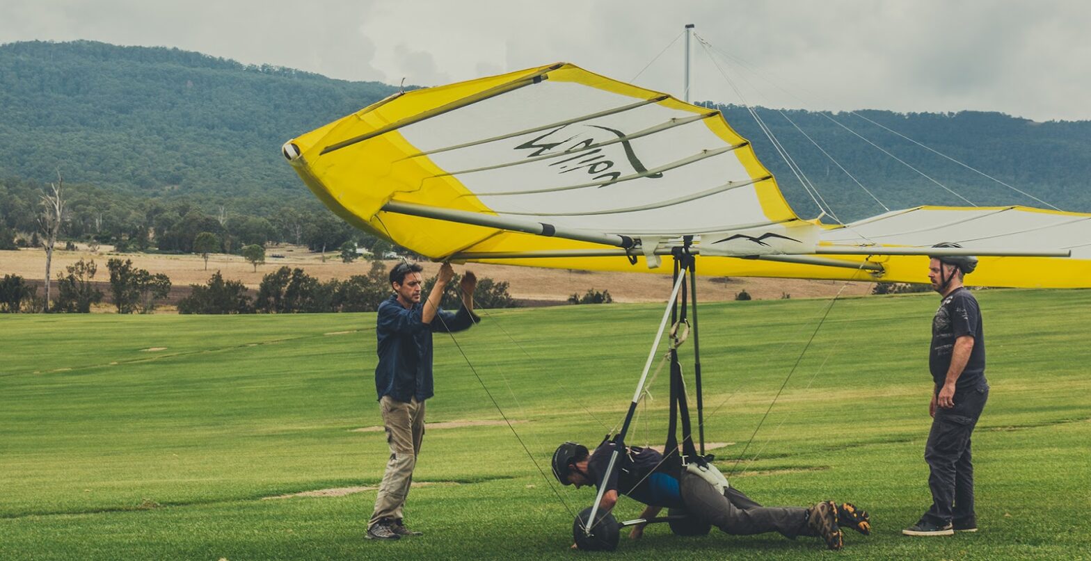 A man prepares to fly a hang glider with two other men helping him