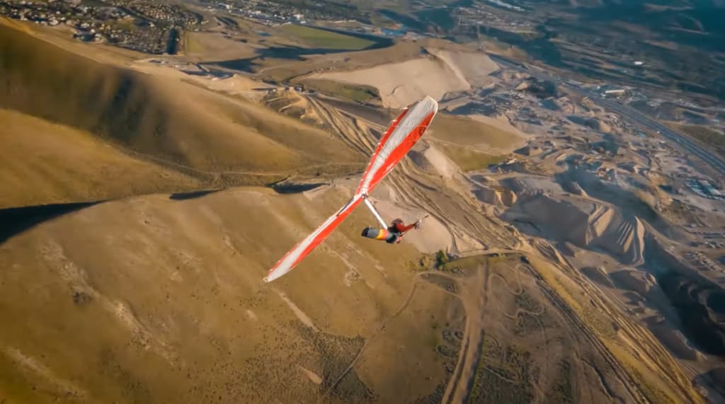 Aerial view of a hang glider soaring over a barren landscape with the shadow of the glider
