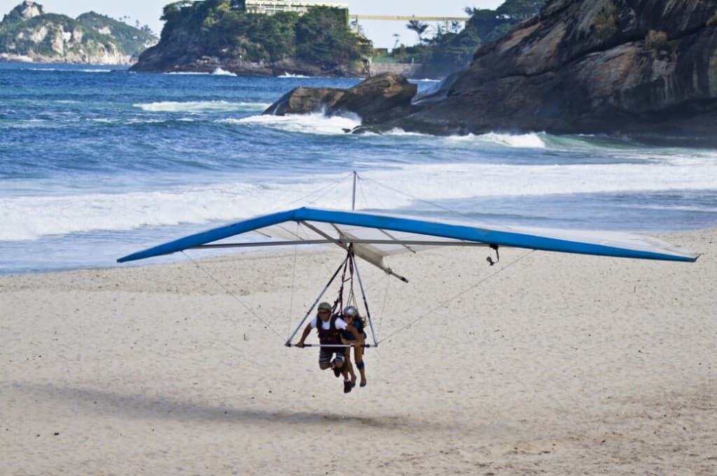 Hang glider landing on a sandy beach with waves in the background