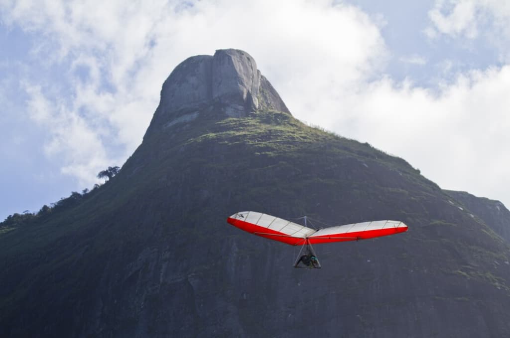 Hang glider soaring in front of a lush green mountain under a blue sky