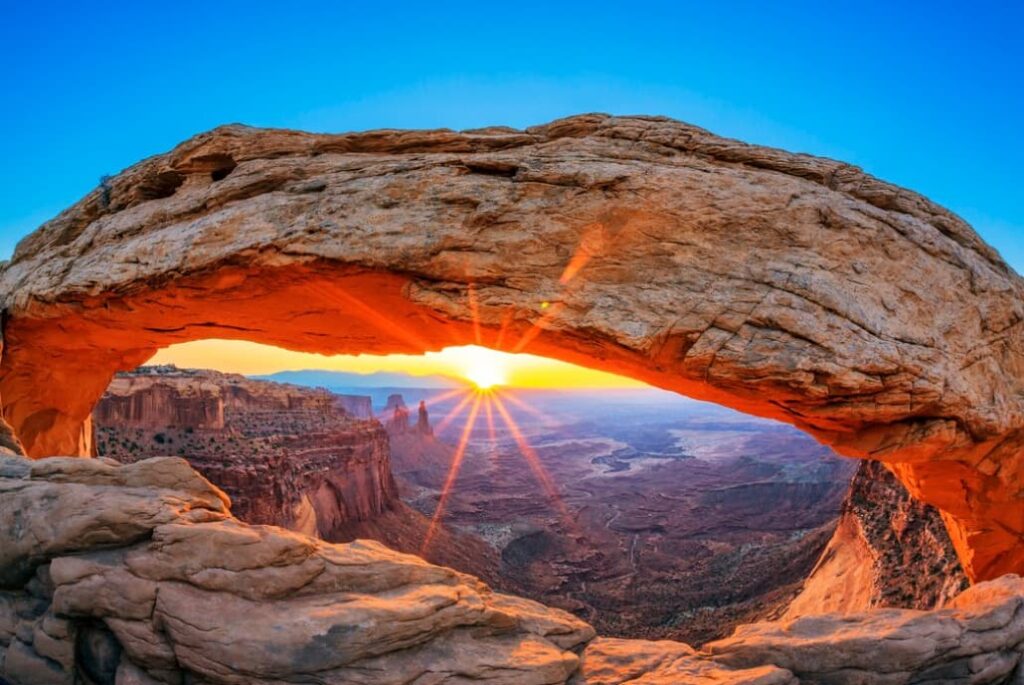 Sunrise viewed through a natural sandstone arch in a desert landscape