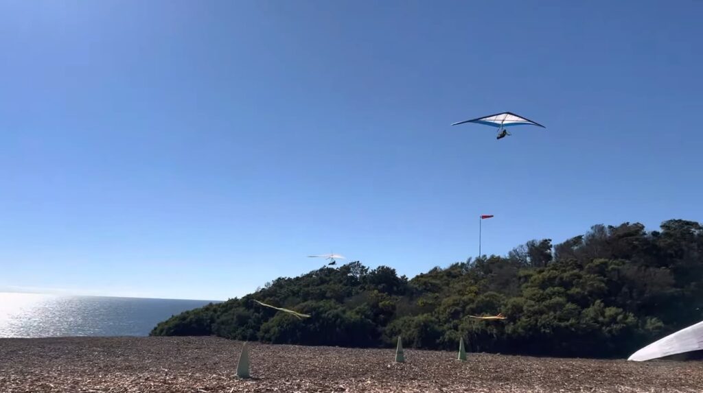 Two hang gliders flying near the coast with a clear view of the ocean and the horizon