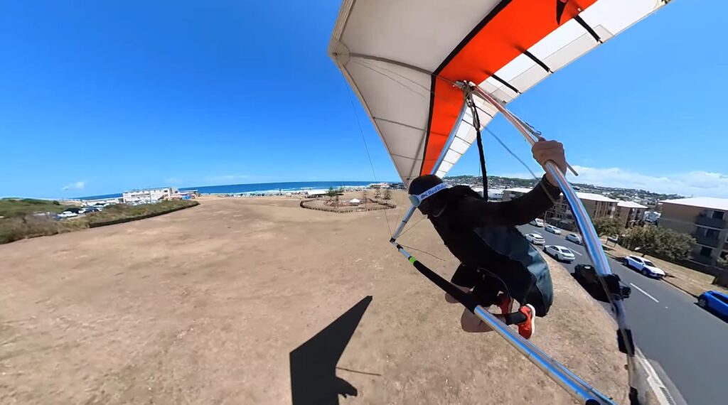 A hang glider pilot taking off from a hillside with a clear blue sky above and a coastal town below